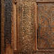 ​​A close-up of an intricately carved wooden panel with calligraphic script intertwined with floral motifs and bordered by geometric star patterns on the right side.