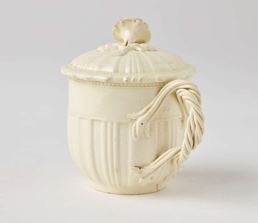  A cream-colored cup with a sculptural swirled handle, and lid with sculpted finial.