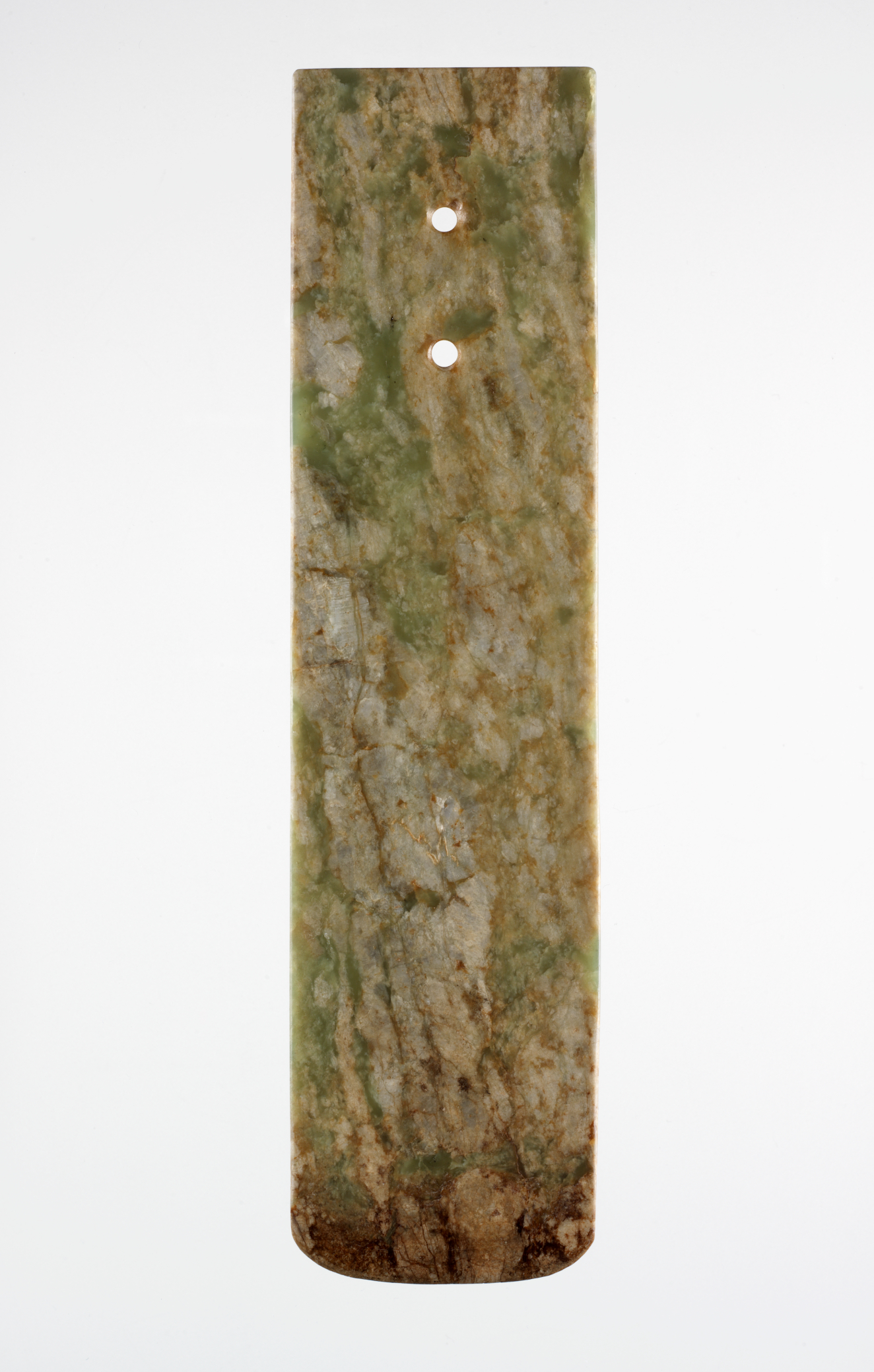 A long, rectangular stone blade with two holes punched below its top edge. The bottom edge is slightly rounded. The blade is a smooth, marbled green and brown texture.
