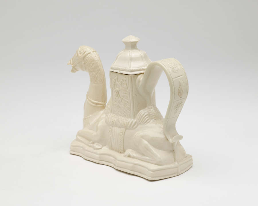 A cream colored teapot in the shape of a camel with a hexagonal lid.