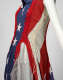 Close-up side view of a dress made from the deconstructed American flag, showing exposed, raw white ribbing and uneven jagged red trim over white starry blue fabric and mesh inserts. 