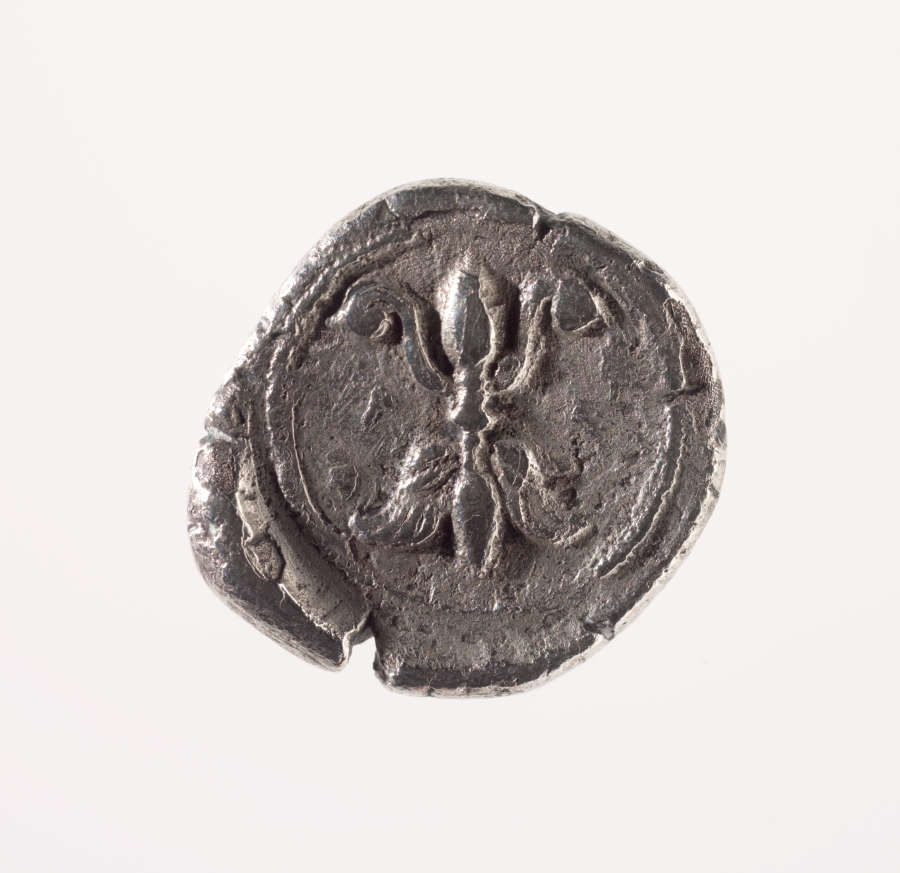 Dull, rough-edged, chipped, squarish silver coin with rounded corners, embossed with the fleur-de-lis motif, framed by a circular border.