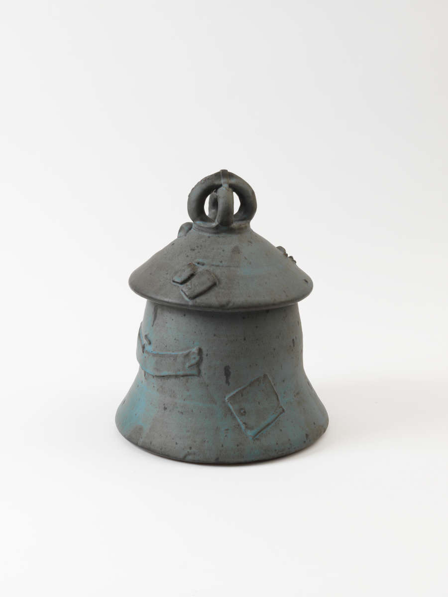 Bell-shaped ceramic jar in blue-gray tones, featuring a domed lid with a looped handle and embossed rectangular patches of varying size and shape scattered across the surface randomly.