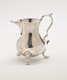 A silver creamer with a sculptural handle and three protruding feet.