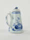 A white and blue teapot with floral decorations, a lid with a small semi spherical finial, spout, and a handle which is located approximately 90 degrees from the spout.