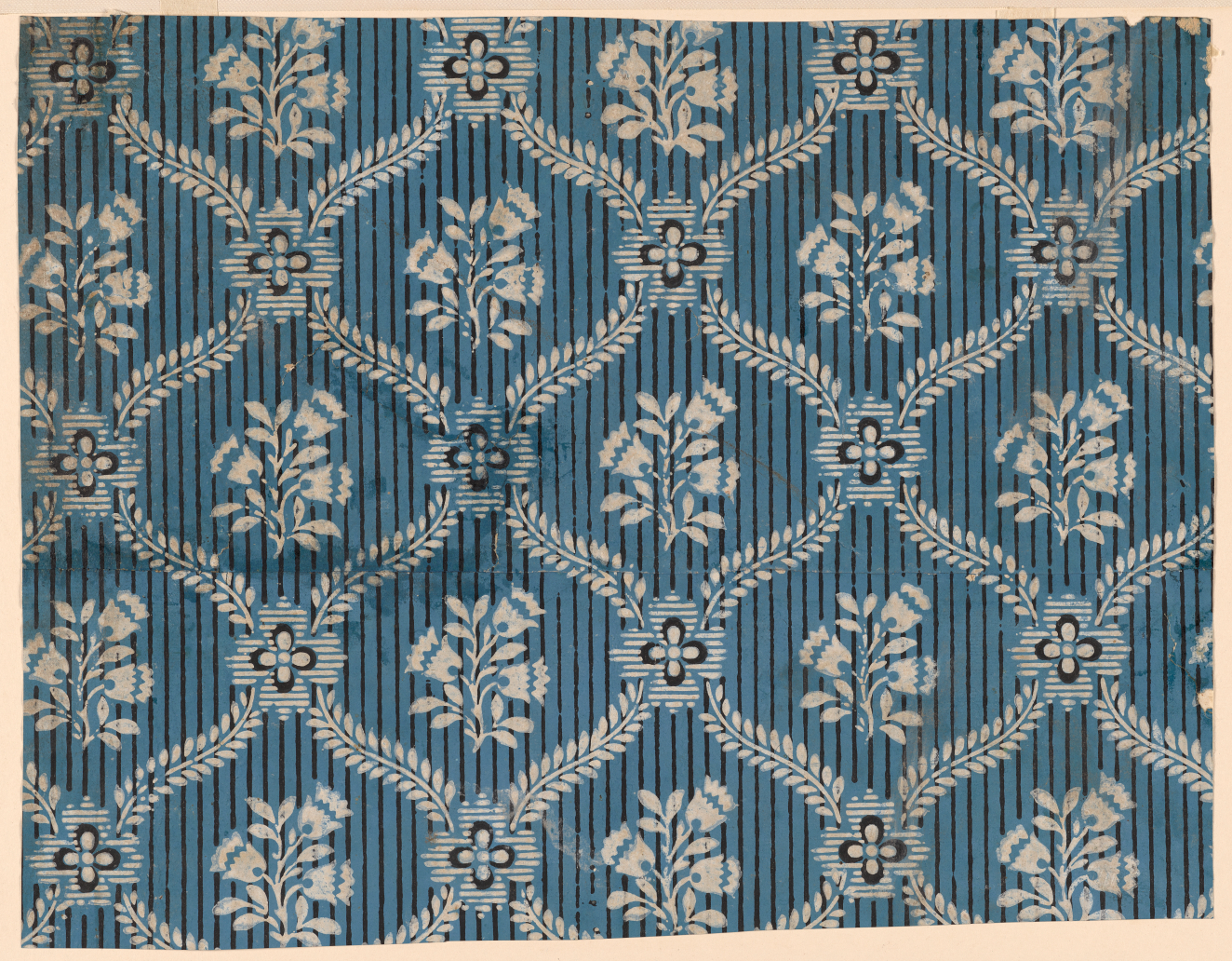 Wallpaper with a repeating pattern made out of white flower bouquets surrounded by white leaves and blue and white petaled flowers repeated vertically and horizontally against a blue and black striped background.