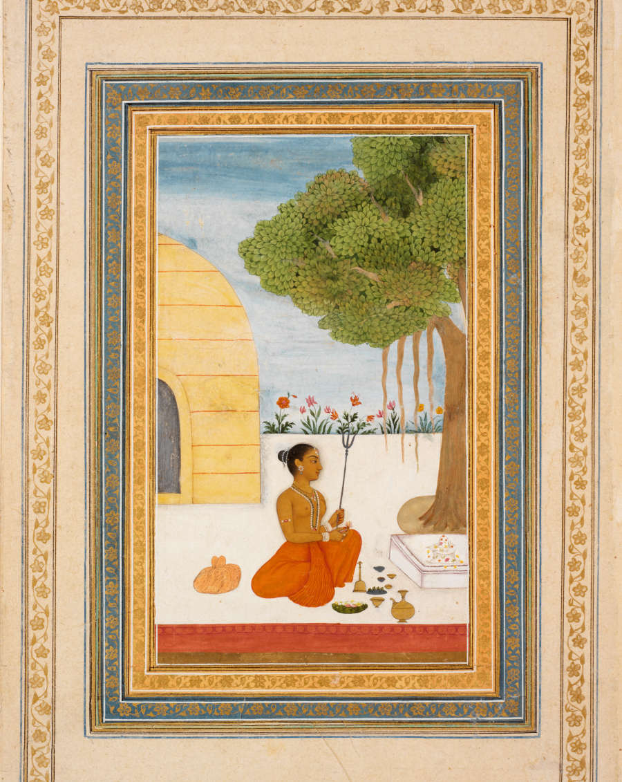 Painting of a topless woman in an orange garment holding a tri-tiered tool, sitting in front of a yellow building and beneath a leafy tree. Various objects surround her.