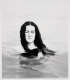 Calm black and white photo of a woman in water, her eyes closed. Her body is submerged below her shoulders, her hair fanned out in the water. 