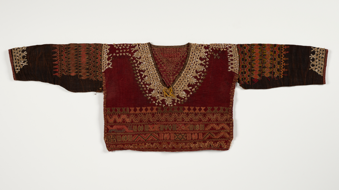 Deep red garment with black sleeves on a white background. Features intricate sequin embroidery around the neckline and geometric patterns  in earth tones along the bottom and shoulders.