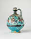 The same blue spherical jug with a slender neck and a handle, decorated with illustrations of humanoid creatures and patterns, turned slightly. It shows signs of wear, breakage, and repair.