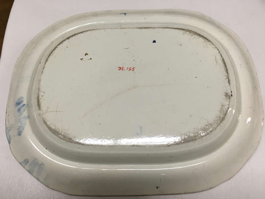 The underside of a white, oval-shaped porcelain dish with a slightly raised rim, with visible scuffs, discoloration, and a red identification number "35.195" at the center.