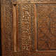 A close up view of a carved wooden panel with intricate calligraphic inscriptions in a vertical band, surrounded by geometric star designs and decorative bands. 