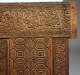 A close up of a carved wooden panel with ornate calligraphic inscriptions along the edges, and geometric designs.  