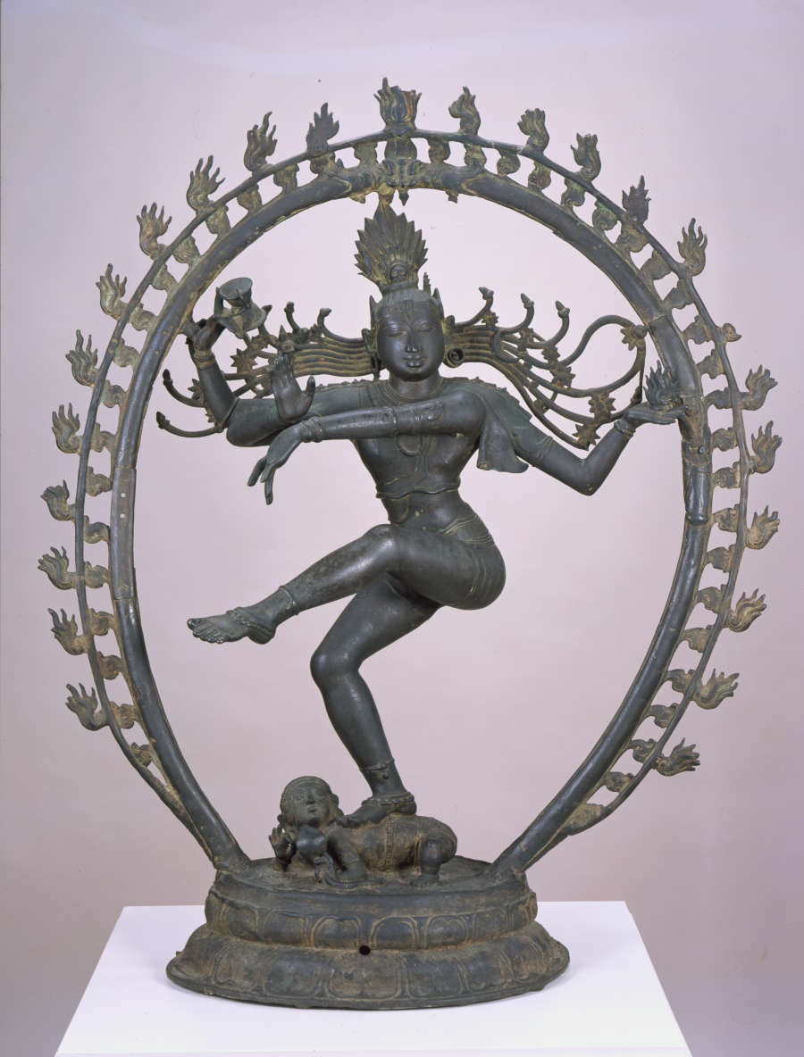 Dark bronze sculpture of a figure with one leg raised and the other bent, and one arm bent upwards and the other extending across its body, surrounded by a sculpted halo.