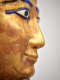 Close-up of a gilded ancient Egyptian face with inlaid eyes and blue eyeliner, viewed from the profile.