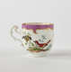 A white teacup with a swirling handle. Gold and pink decoration at top edge. Central design features two birds on a branch.