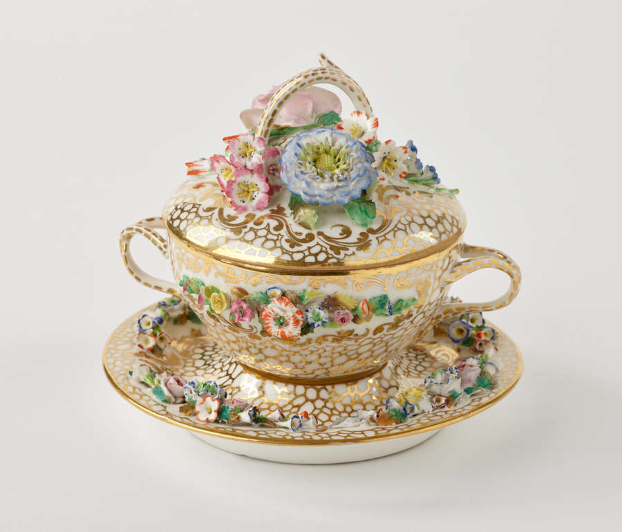 A two handled covered bowl and fitted saucer. The decorations are gold, pink, green and are floral.