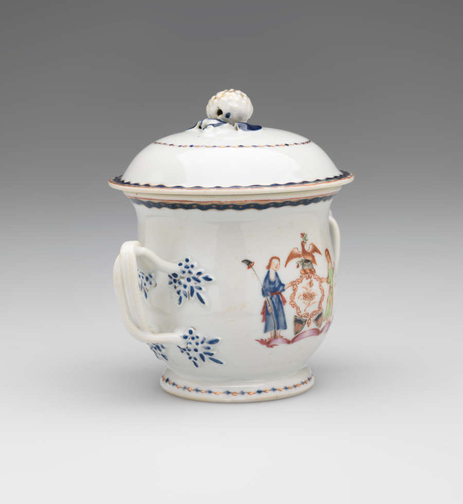 A white vessel with two symmetrical handles with blue decorations, heraldry imagery, two figures with light hair. One holding a staff and the other is blindfold and holding scales.
