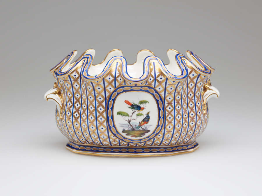 An open vessel with a deeply scalloped rim. A central decoration of two birds and a tree is surrounded by vertical bands of blue with gold diamond shapes.