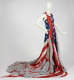 Sleeveless dress designed from a red, white, and blue stars-and-stripe patterned material resembling the American flag with sheer grey fabric cascading to the floor in a sweeping train. 