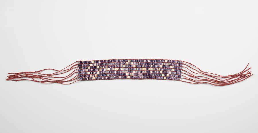 Purple and white beaded belt with a geometric diamond pattern and loose maroon warp thread ends.