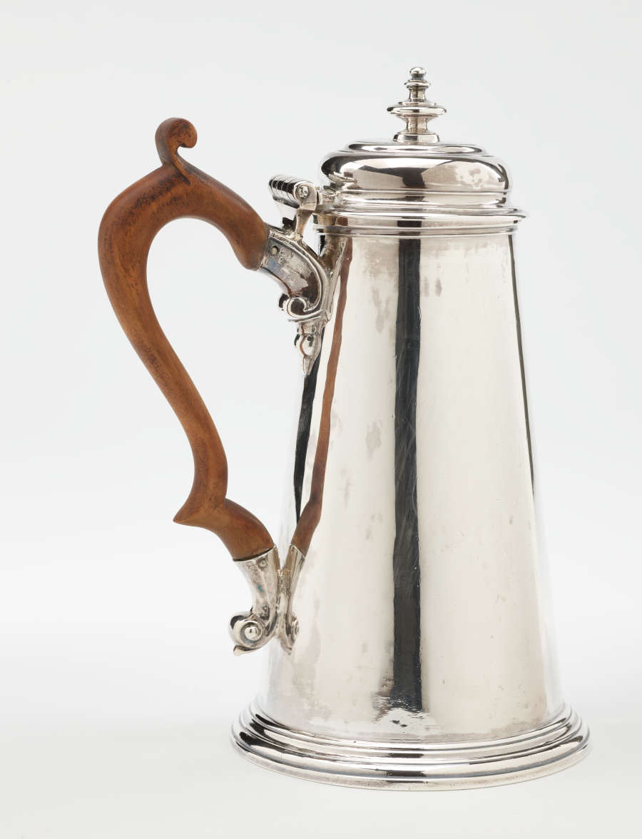 A silver chocolate pot with a spout, hinged lid, and fruitwood handle that is 90 degrees from the spout.
