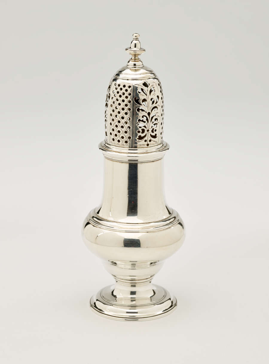 A silver vessel with a foot, rounded body that goes to a cylindrical top half, and the lid is perforated with small holes and floral cutouts.