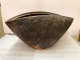 Side view of a clam-shaped bowl in storage. Its body is dark brown with vertical etching and speckled with lighter earth tones. 