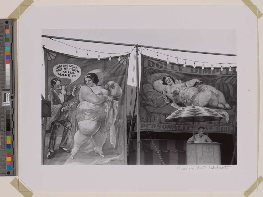 Grayscale photograph of two large banners. The left-side banner shows a fat woman, barely dressed, and a thin man in a suit saying “Just one more bolt of cloth will make it.” The right-side banner depicts the woman lying sideways, with text reading “Dolly Dimples” and “Personality Fat Girl.”