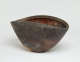 Back view of a brown clam-shaped stone bowl with shell-like etchings on its exterior and a red-orange interior. Its rim dips at the sides forming a wave-like shape.