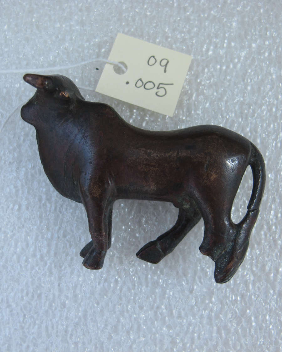Side view of a black standing bull with its characteristic tail and dewlaps against a styrofoam white background. Above it is a white tag that reads “09 .005”.