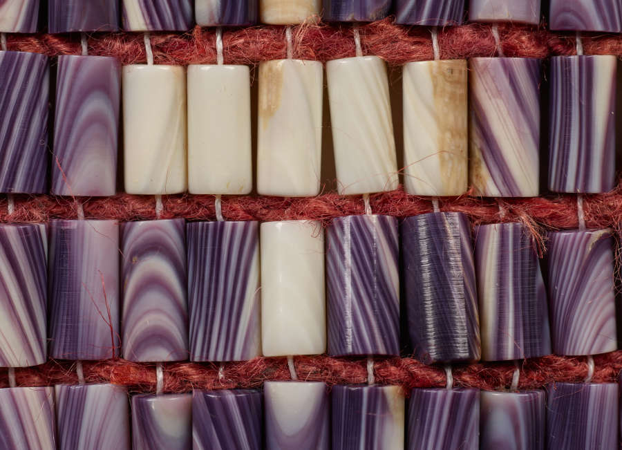 Close-up of the patterned beaded belt patterned with striated white shells within rows of striated purple shells, woven together with maroon and white thread.
