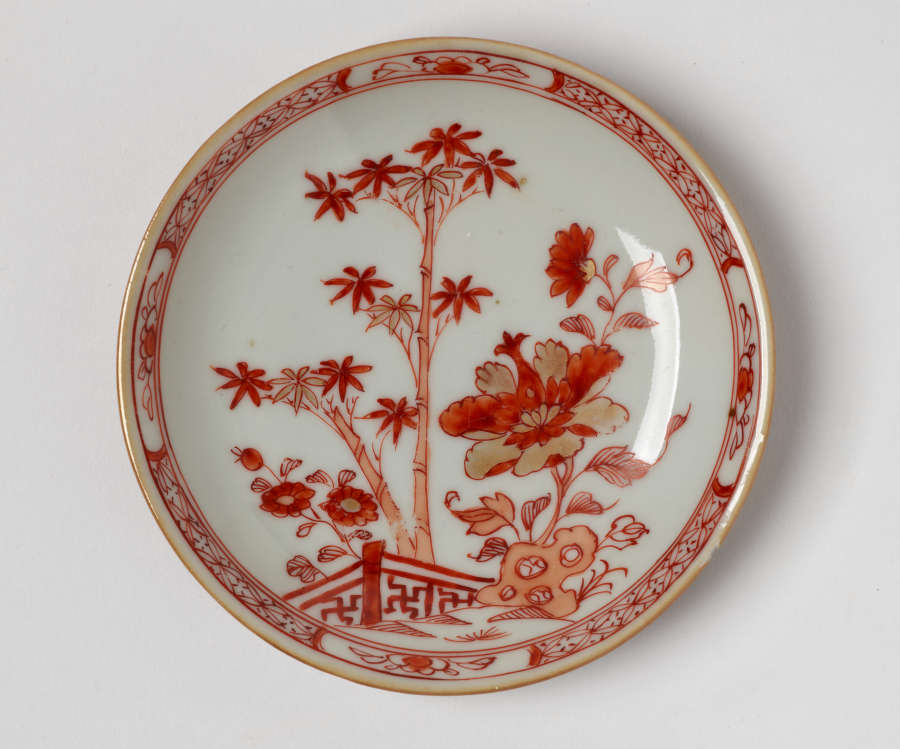  A cream colored plate with red and gold floral, structural, and abstract decorations.