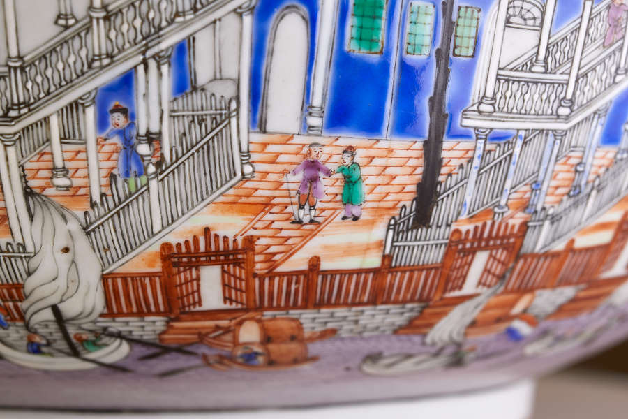 A painted ceramic scene depicting a vibrant courtyard scene with three figures, one on an orange tiled balcony, and the two others in the central courtyard, surrounded by intricate fencing.