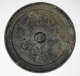 Black, round and corroded back of a handless mirror, embellished with a thick raised border, concentric illustrations and a domed center. It also has a greenish-yellow patina.