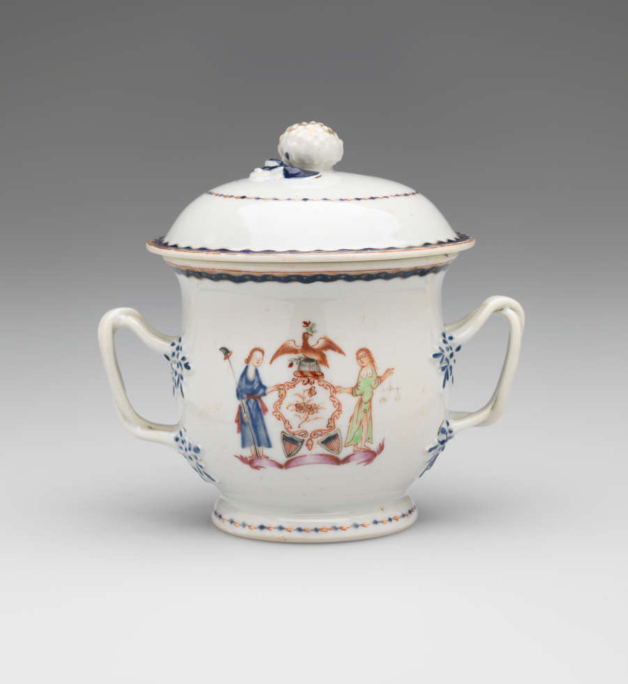 A white vessel with two symmetrical handles with blue decorations, heraldry imagery, two figures with light hair. One holding a staff and the other is blindfold and holding scales.
