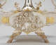 A silver oval relief panel depicting a robed man surrounded by cherubs and vines and swirling drapery, enclosed in a gold-trimmed frame attached to a tray elevated by ornate legs.