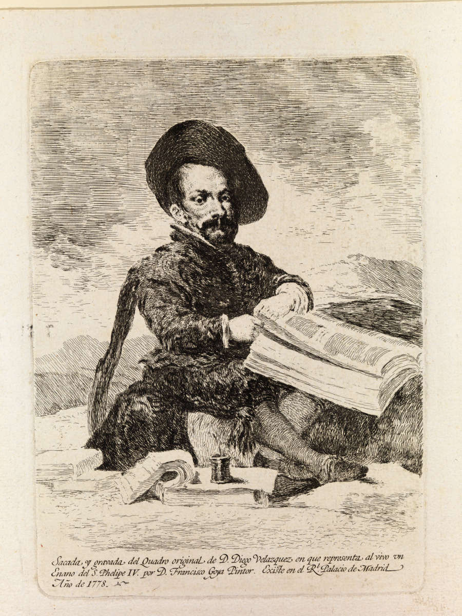 In an etching on beige paper, a little person sits cross-legged among books, papers, and a pot of ink. He wears an 18th-century suit and wide-brimmed hat. Text at the bottom is in Spanish. Translated into English reads: “Taken and captured from the original painting of Diego Velazquez which represents the Dwarf of King Philip IV by Francisco Goya, [illegible] in the Royal Palace of Madrid, 1773.”