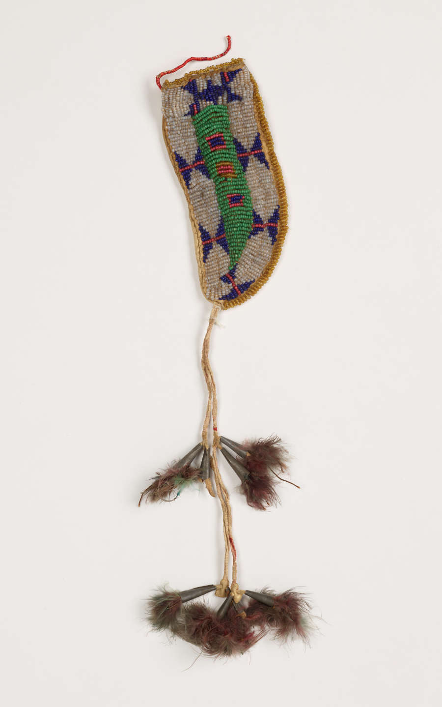 A beaded knife case with a thread coming from the tip, connecting to two sets of brown-red tassels. The case features a beaded green, blue, and orange geometric motif.