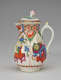 A white milk jug with a handle, lid, and spout with green, red, blue, pink, yellow, gilded decorations,and two vignettes; an animal and a table, vessels, and floral elements.