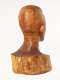 Three quarter back view of a glossy wooden bust depicting the head of a  male figure. The wood features long vertical cracks, carving marks and color variation.