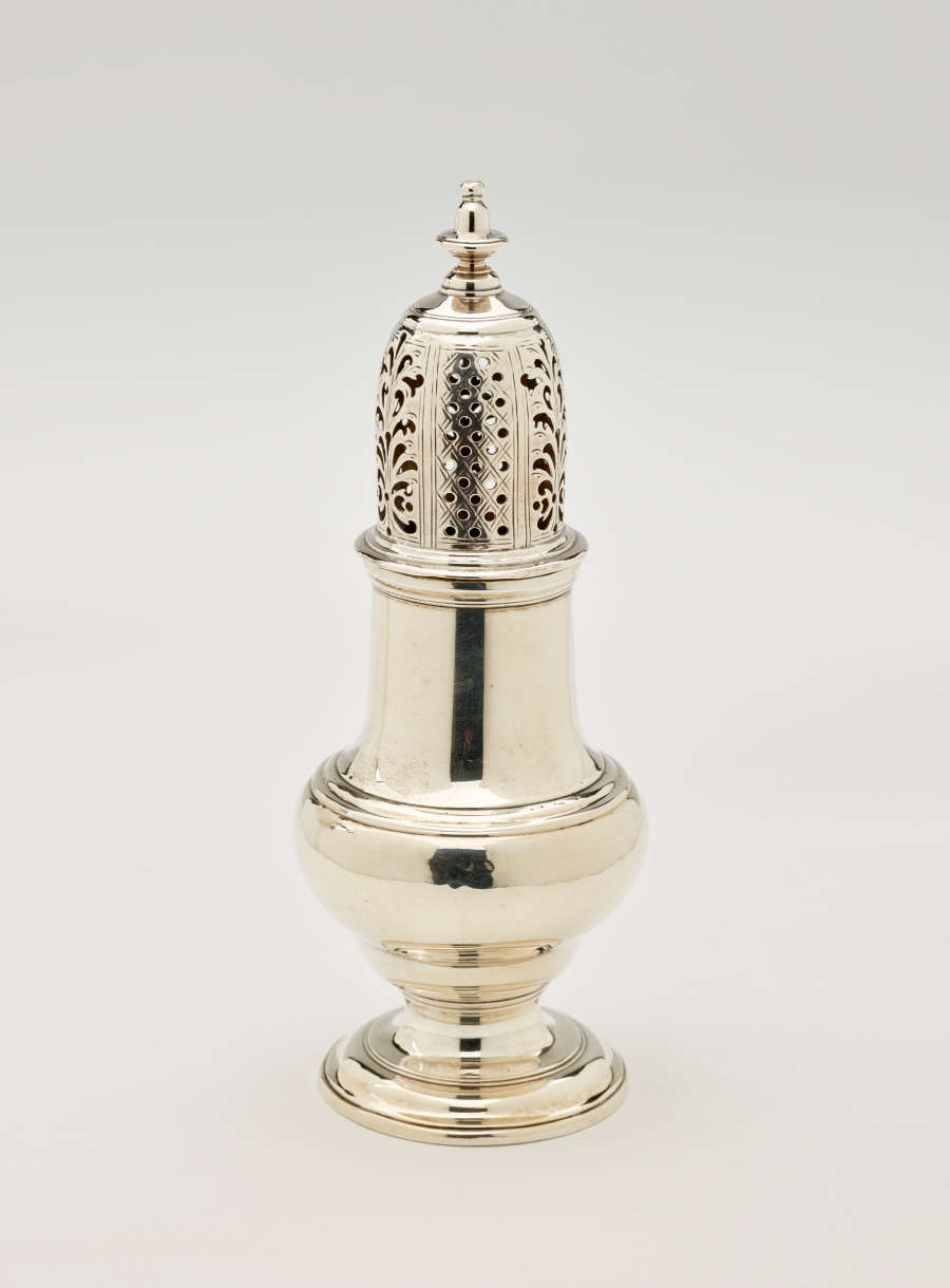 A silver vessel with a foot, rounded body that goes to a cylindrical top half, and the lid is perforated with small holes and floral cutouts.