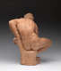 Realistically carved terracotta sculpture depicting the back of a muscular man leaning over while sitting, his bent arm supporting him against a rough pedestal he sits atop.