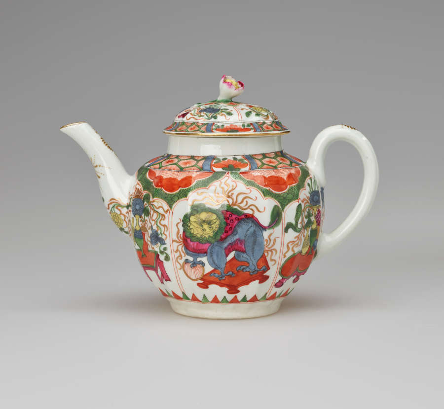 A white teapot with a handle, spout, lid and finial, with green, red, blue, pink, yellow and gilded decorations. The main vignite shows a dragon on a table.