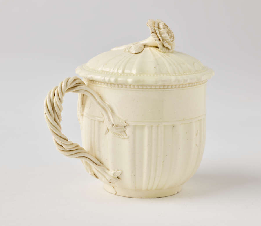  A cream-colored cup with a sculptural swirled handle, and lid with sculpted finial.