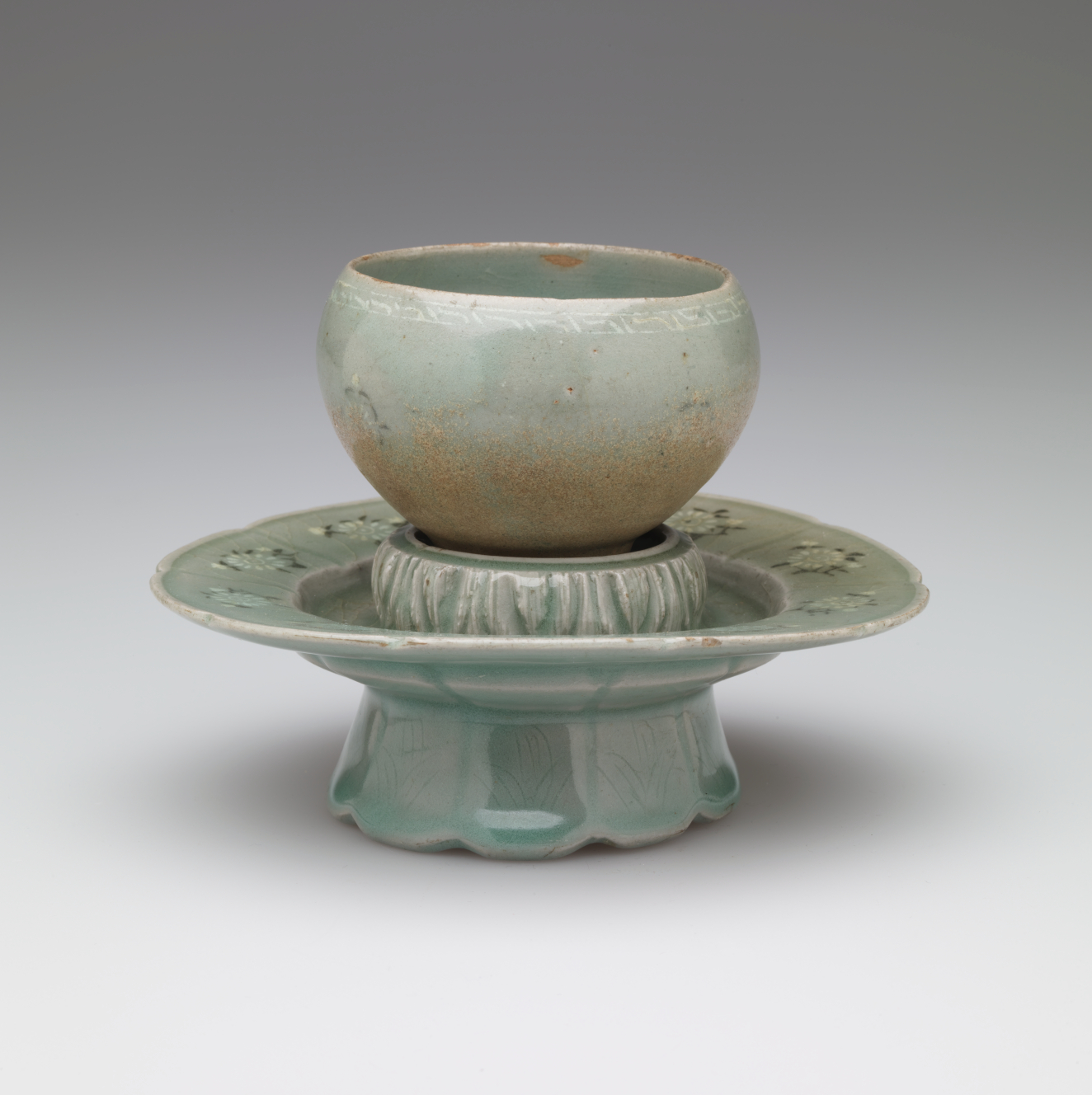 A rounded vessel sitting on a pedestal with a scalloped foot.