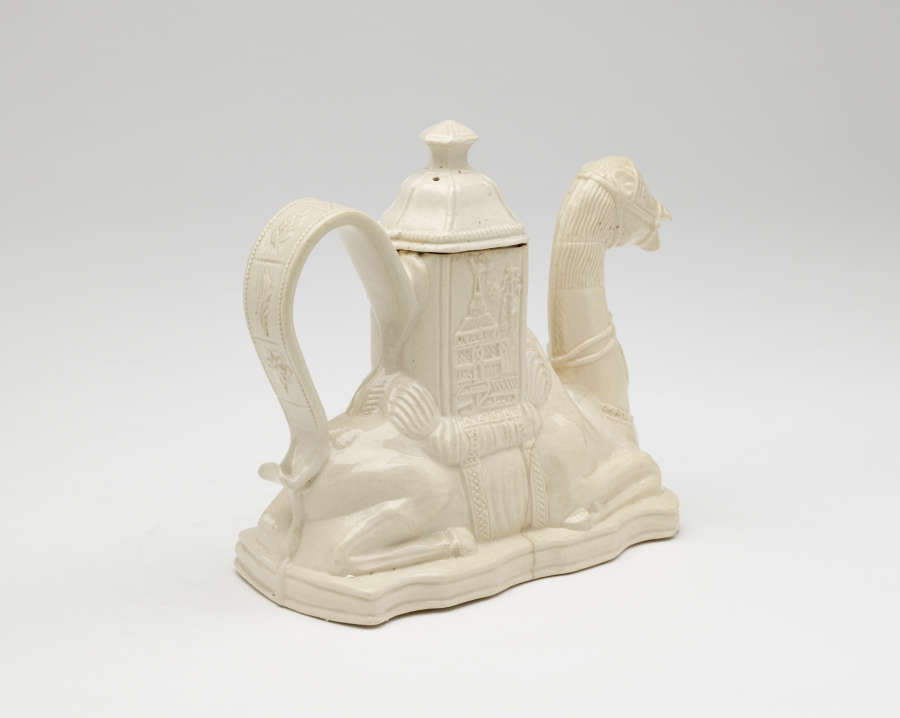 A cream colored teapot in the shape of a camel with a hexagonal lid.