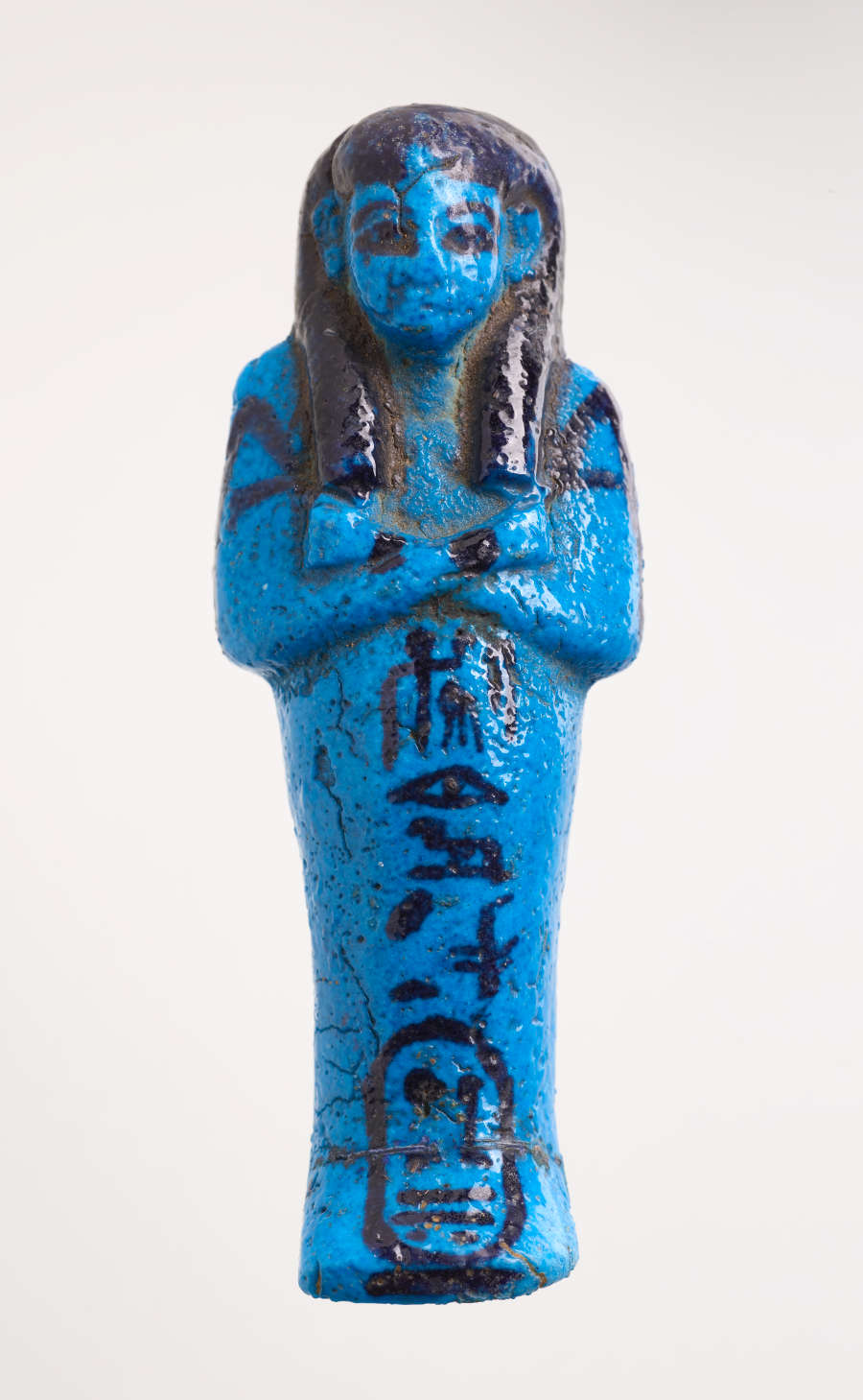 Front of a blue sculpture of a mummy-like figure with hands laid on its chest, with black detailing and hieroglyphic writing trailing down the length of its body laid horizontally.