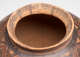 A close-up of a ceramic jar's wide, unglazed mouth, with evidence of wear and decorated with faded brown and red geometric patterns.