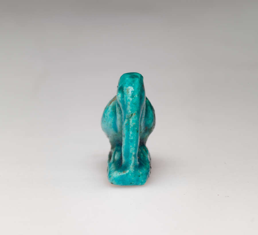 Front of a turquoise amulet, of a crouching pelican-like bird with a long beak pointed downwards, head tucked into its neck, where there is a small loop.